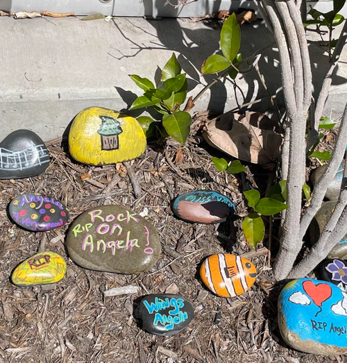 River rocks painted with messages saying Rock On Angela, RIP, miss you, wings Angela